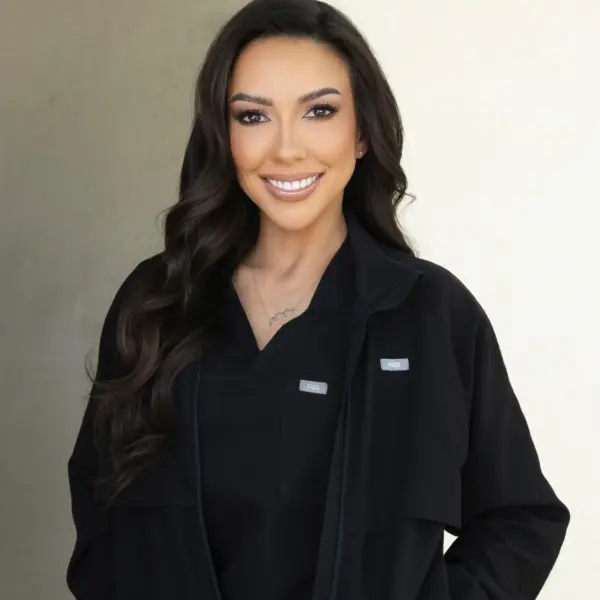 Close-up portrait of a smiling woman with long dark hair, wearing a black jacket, neutral background