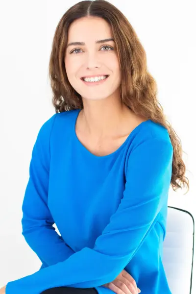 Smiling woman with long brown hair in a bright blue top, posed against a white background.